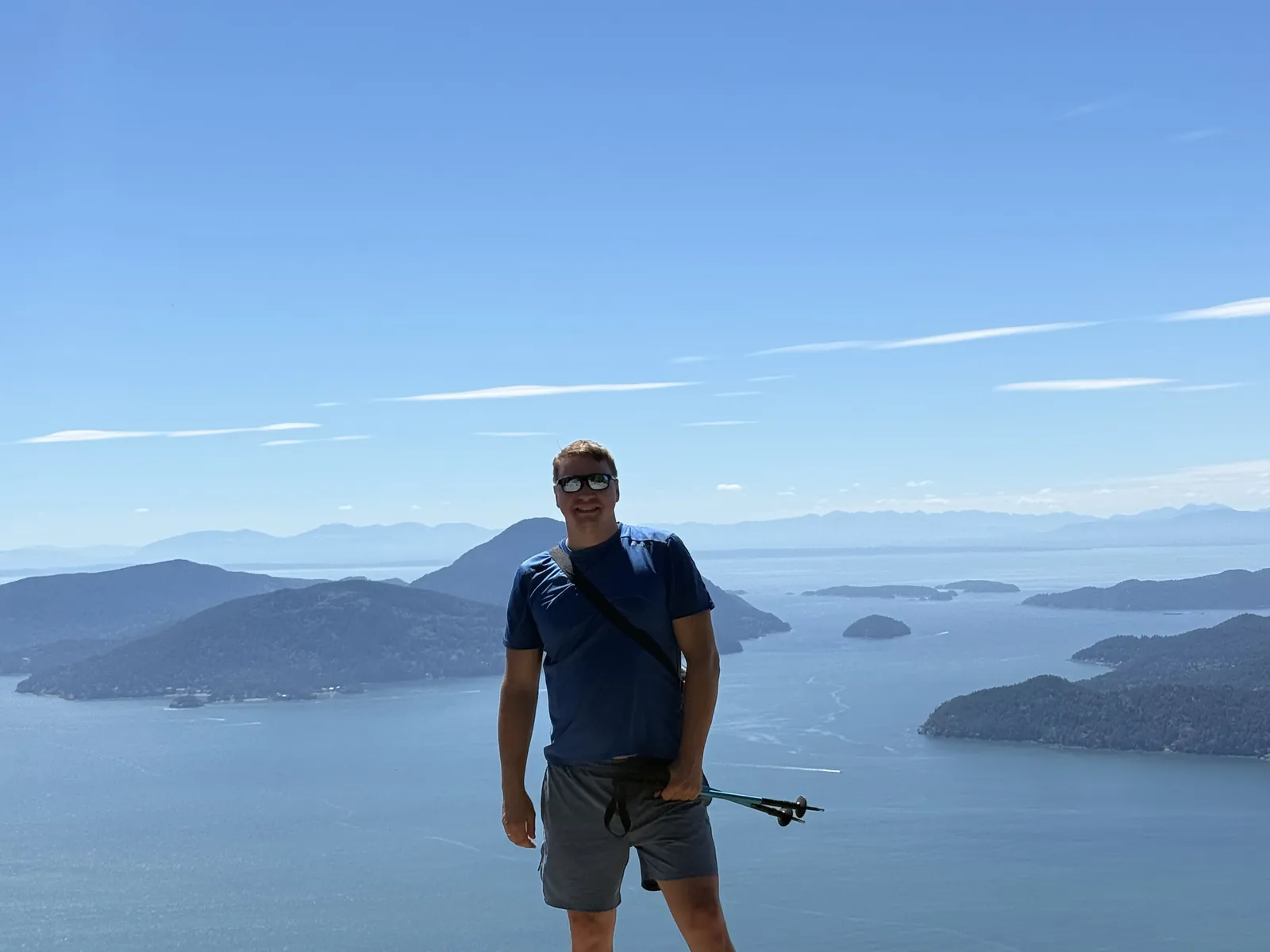 A WP Support BC team member smiling on a rocky coastal summit above islands and open water in British Columbia