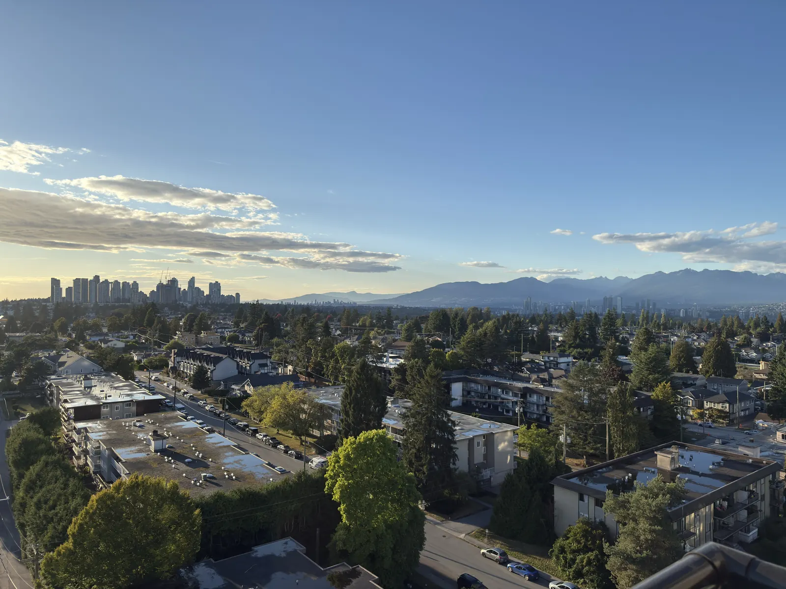 Clear-day view over a Metro Vancouver neighbourhood toward the North Shore mountains and a distant city skyline